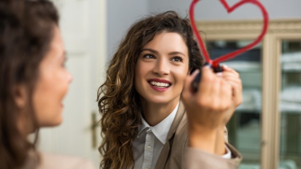 Businesswoman is drawing heart with lipstick on the mirror while preparing for work