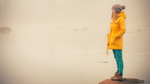 young woman facing water outside on rock