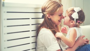 Matka z córką siedzą koło okna bawiąc się ze sobą, całując i przytulając