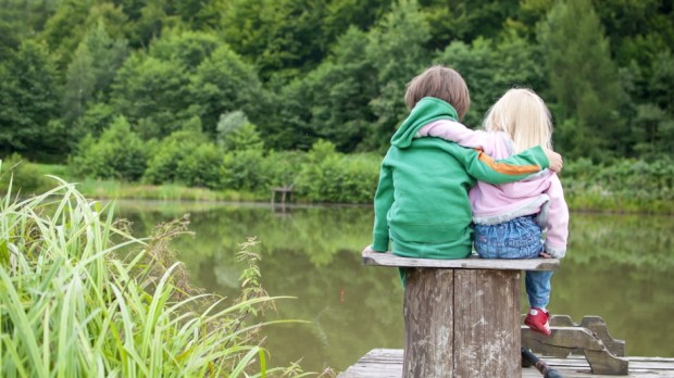 Two little children hug each other and look a the lake view