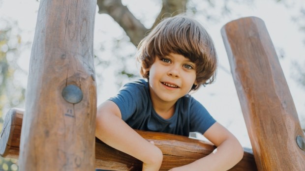 portrait of a smiling little brunette boy in a blue T-shirt playing outdoors