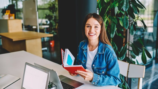cheerful female student with education notepad sitting at table desktop