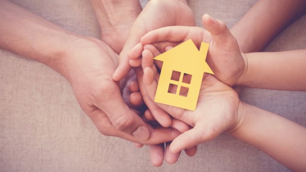 Adult and child hands holding paper house