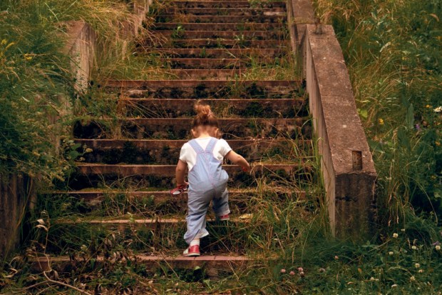 A little girl, 2 years old, with a ponytail and in a jumpsuit, climbing up the steps of the old stone