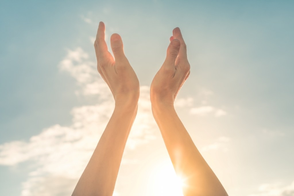 Worshiping hands up to the sun light sky feeling the warm rays of sunshine