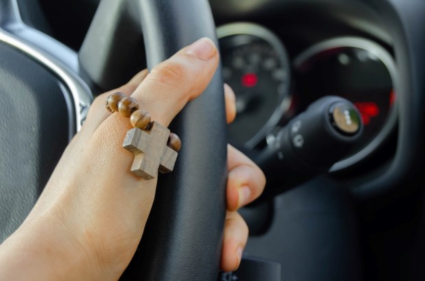 A small wooden rosary on a finger, while hand driving the car