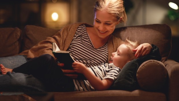 Family before going to bed mother reads to her child son book near a lamp in the evening