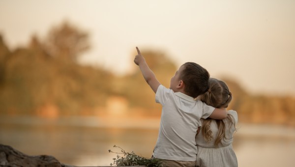 A BOY AND A GIRL SIT ON THE RIVER SHORE IN THE SUMMER IN THE PARK AT SUNSET