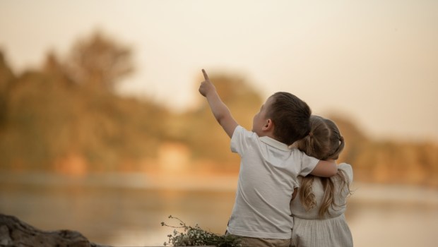 A BOY AND A GIRL SIT ON THE RIVER SHORE IN THE SUMMER IN THE PARK AT SUNSET