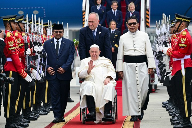 Pope Francis waves from a departing vehicle following his arrival at Soekarno-Hatta International Airport in Jakarta on September 3, 2024